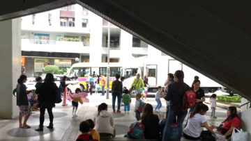 校車站呈現一片熱鬧的景象，令那位埋首於手機的小男孩顯得格格不入